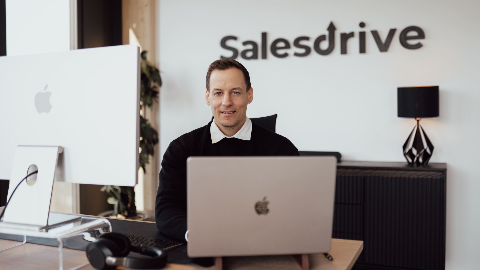 Alexander am Schreibtisch im SalesDrive Büro vor dem Logo