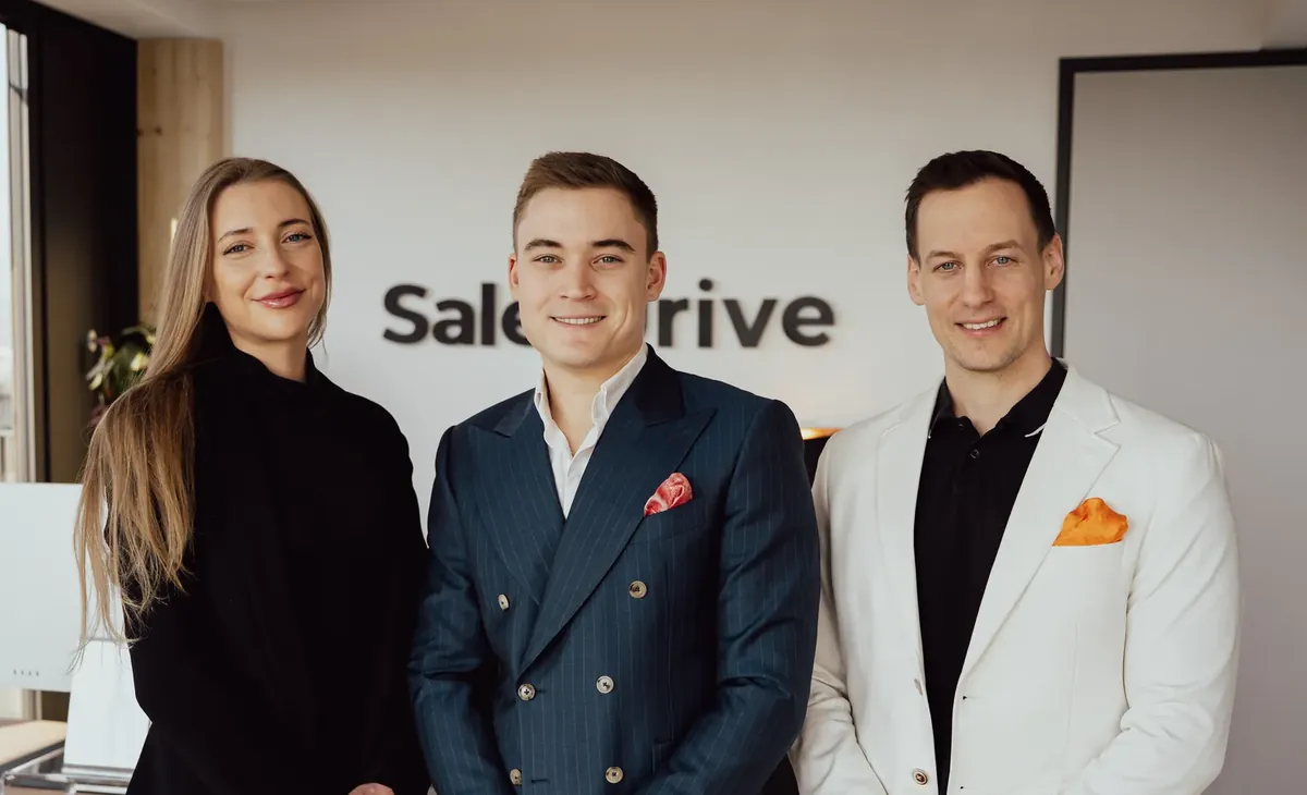 Drei Menschen aus dem SalesDrive-Team vor der SalesDrive-Wand im Büro in Wien